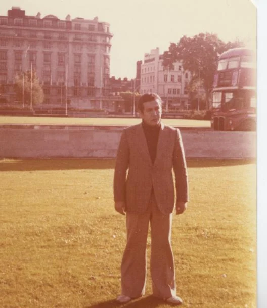 Kamal Ruhayyim steht auf einer Rasenfläche, Gebäude und ein Bus im Hintergrund.