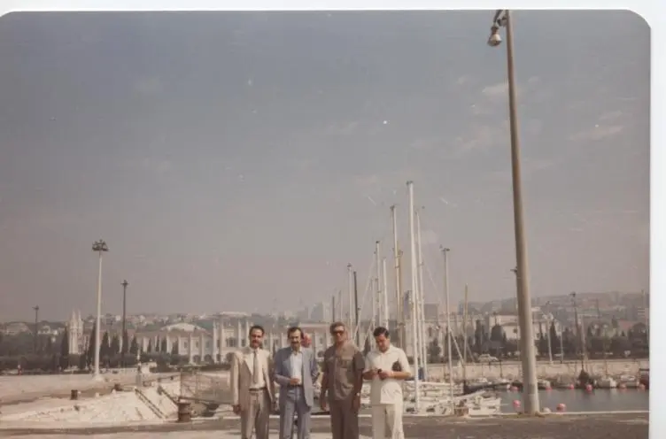 Une ancienne photo couleur de quatre hommes près d’une marina de voiliers à Belém, avec le monastère des Hiéronymites au fond.