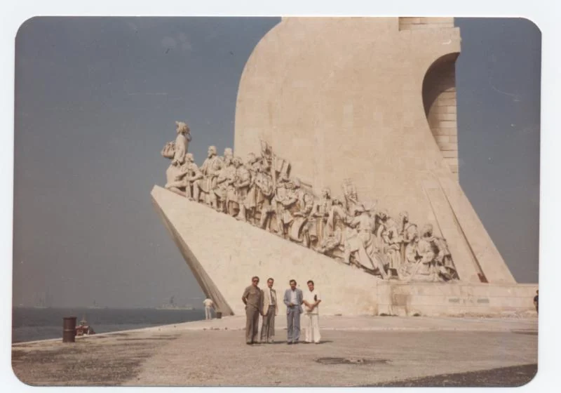 Vier Männer stehen vor einem großen Denkmal am Wasser in Lissabon.