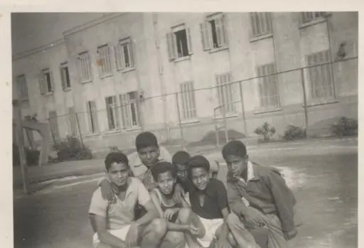 Une ancienne photo en noir et blanc d’un groupe d’écoliers assis serrés dans la cour du lycée de Maadi, devant le bâtiment de l’école.