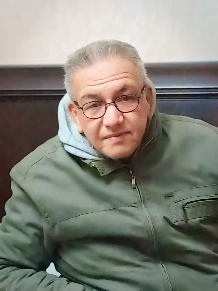 صورة شخصية للروائي المصري كمال رُحيّم مبتسمًا ويرتدي معطفًا أخضر ونظارة