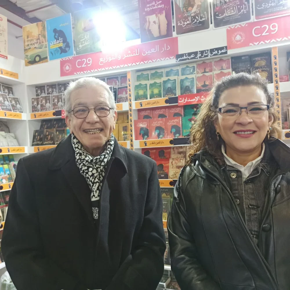 كمال رُحيّم يقف مبتسمًا بجوار الكاتبة فاطمة ناعوت أمام أرفف الكتب في معرض.