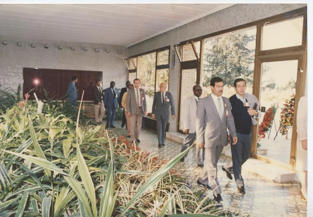 Men in suits walking through a building with indoor plants.