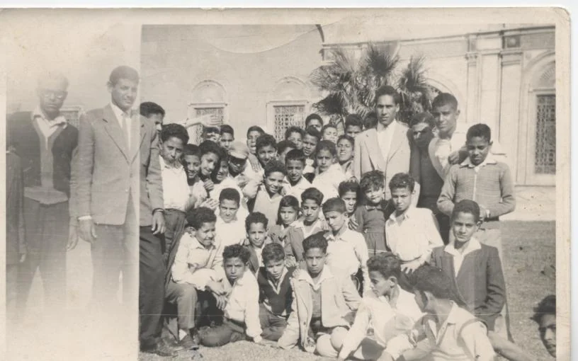 صورة جماعية بالأبيض والأسود لتلاميذ مع معلميهم أمام مبنى تاريخي.